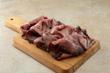 A view of a wood board of roast beef deli slices.