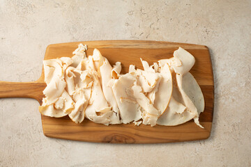 A top down view of a wood board of chicken breast deli slices.