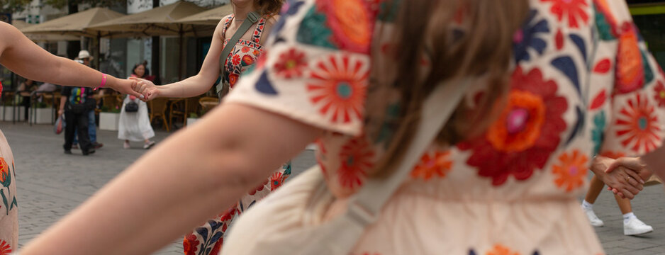 Woman in embroidered dress twirling arm, capturing flowing sleeve detail and delicate stitchwork during joyful folk dance at outdoor festival, sunlight highlighting texture and movement