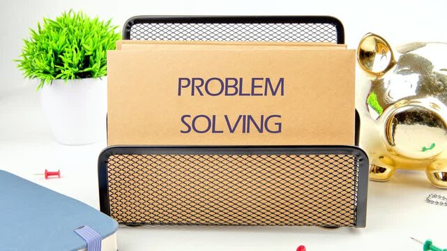 A folder labeled PROBLEM SOLVING slowly changes color and clarity. It sits on a white desk with a piggy bank, a plant, a notebook, and tacks near