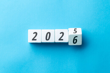 Transition from 2025 to 2026 concept with white cubes flipping on a blue background. Minimalist flat lay symbolizing new year goals, business planning, and future progress.