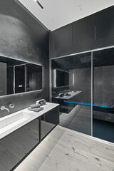 Modern black bathroom interior with parquet flooring, sink cabinet in the left foreground and glass shower enclosure in the background, minimalist contemporary design
