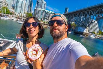 Tourists taking selfie with donut in vancouver harbor with cityscape in background