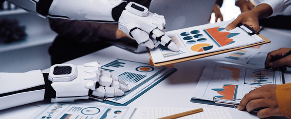 A robotic arm assists a group of professionals in analyzing data, showcasing the integration of technology and human collaboration in a dynamic office setting.Noogenesis