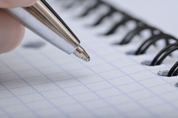 Close-up of a hand with a pen, writing something in a squared notebook