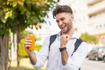 Fototapeta premium Young handsome man holding an orange juice at outdoors celebrating a victory