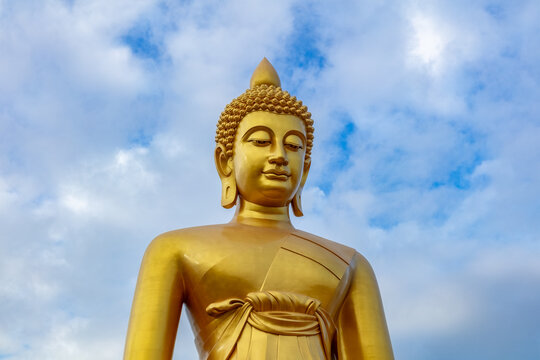 Giant golden Buddha statue at Wat Paknam, Bangkok, Thailand. Cloudy blue sky in the background. Measuring 69 meters tall (226 feet, it is the largest Buddha statue in Bangkok. 
