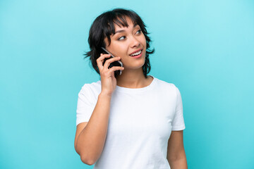Young Argentinian woman isolated on blue background keeping a conversation with the mobile phone with someone