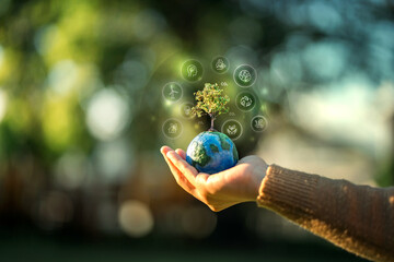 Close up of a hand holding a small globe with a growing tree surrounded by digital ESG icons for sustainability, environmental protection, and green energy concept