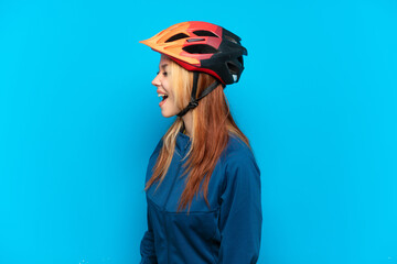 Young cyclist girl isolated on blue background laughing in lateral position
