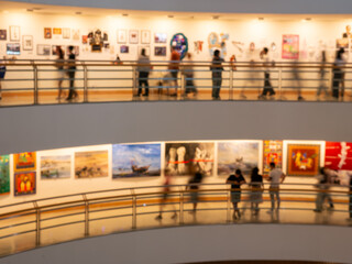 Blurred background of people standing on a balcony viewing art gallery exhibits along a white wall, abstract culture and leisure concept.