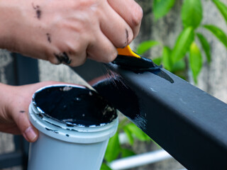 Close up shot of a person's hand painting a black anti-rust protective primer or paint onto a metal frame using a small brush, home repair and maintenance concept.