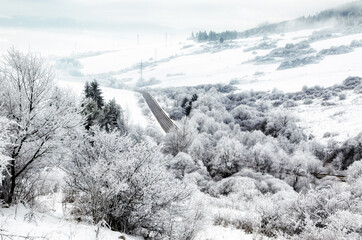 Winter road winding through frosty valley with snow covered trees and hills