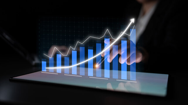 This image depicts a professional analyzing a digital financial graph with blue bars and a white trendline on a touchscreen device, showcasing growth and data analysis. Impute - Powered by Adobe
