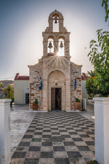 Stone church in Panormos village on Crete with bell tower, sunburst light and traditional Greek architecture