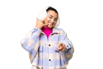 Young woman wearing winter muffs over isolated chroma key background making phone gesture and pointing front