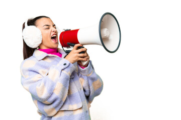 Young woman wearing winter muffs over isolated chroma key background shouting through a megaphone
