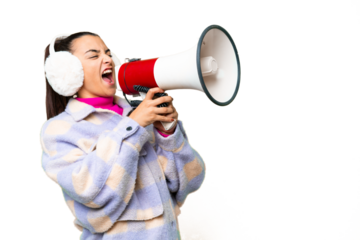 Young woman wearing winter muffs over isolated chroma key background shouting through a megaphone