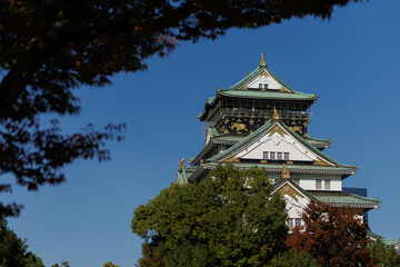 Naklejka premium The Osaka-jo Castle Tower in Japan, with White Walls and a Green Roof, Against a Clear Blue Sky