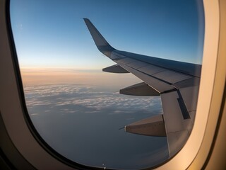 View of an airplane wing through the window during flight above the clouds at sunrise