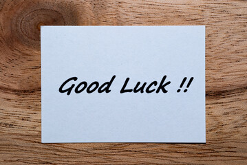 The words "Good Luck" are written on a piece of white paper on a wooden table.