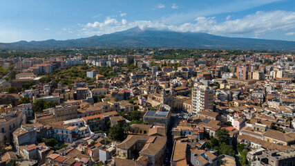 Obraz premium Aerial view of the historic center of Acireale, in the province of Catania, Sicily, Italy. In the background, on the horizon, Mount Etna looms in silhouette, dominating the panorama. It is a sunny day