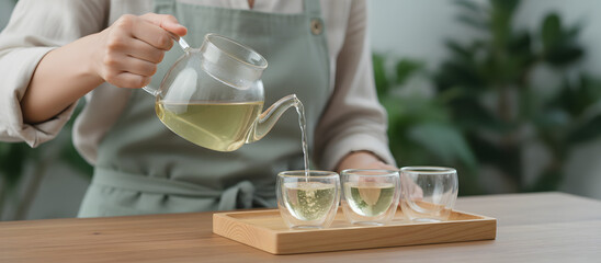 Woman pouring green tea into glass cups on wooden tray indoors  