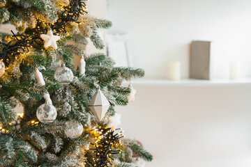 Snowy frosted Christmas tree branches decorated with white ornaments, warm glowing string garland lights, illumination on background. Soft winter atmosphere for holiday backdrop and seasonal designs