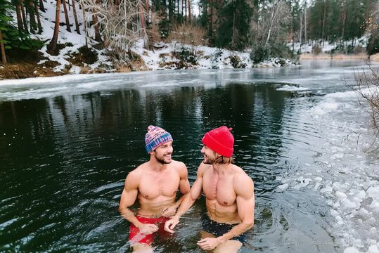 Two friends wearing wool hats bathing in a frozen lake in winter
