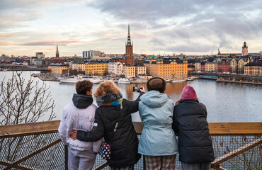 Family on winter vacation in Stockholm admiring panoramic cityscape and taking a cheerful selfie from scenic viewpoint overlooking historic waterfront and colorful buildings
