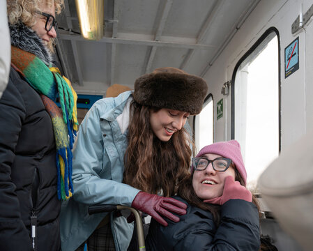 Three women traveling by ferry in Stockholm, supporting woman with cerebral palsy during joyful winter journey