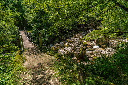 Wooden bridge over mossy riverbank leading to hidden Sunik Waterfalls in Slovenias Soca Valley