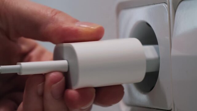 Close-up footage of hand inserting electrical plug into wall socket, connecting power source for electronic devices. . High quality 4k footage