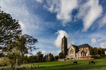 Green meadow with grazing horses and a majestic church under a blue sky with moving fluffy clouds.