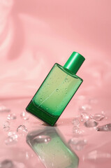 Elegant green glass perfume bottle with water droplets on pink background