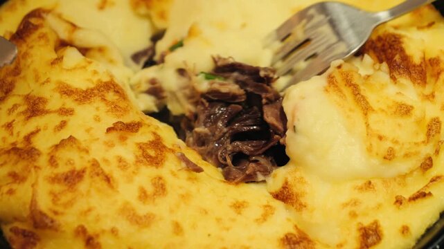 A man using a knife and fork cuts a potato and duck pie close up, Duck Parmentier or Parmentier de Canard is a classic, hearty casserole from France, using shredded duck confit under a creamy mashed