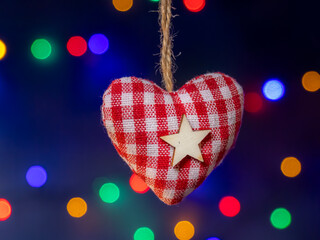 Red Gingham Heart Ornament With White Star Hanging Against Colorful Christmas Lights