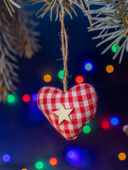 Red Gingham Heart Ornament With White Star Hanging Against Colorful Christmas Lights