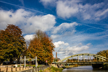 Urban river landscape. Arched bridge over canal, autumn trees and old industrial chimney.