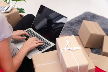 E-commerce Orders: A person diligently works on a laptop, surrounded by wrapped packages, possibly managing an online retail store or handling shipping tasks.