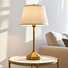 A gold-toned table lamp with a pleated white shade sits on a round light-colored side table, in a bright living room