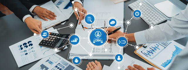 A dynamic business meeting scene showing teamwork around a table with a focus on CRM strategies. Digital links illustrate connectivity and collaboration in a corporate setting. Amity