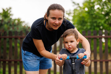 Fototapeta premium Mother teaching son to ride a scooter
