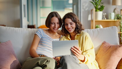 Besties enjoy online shopping looking tablet at couch closeup. Smiling women