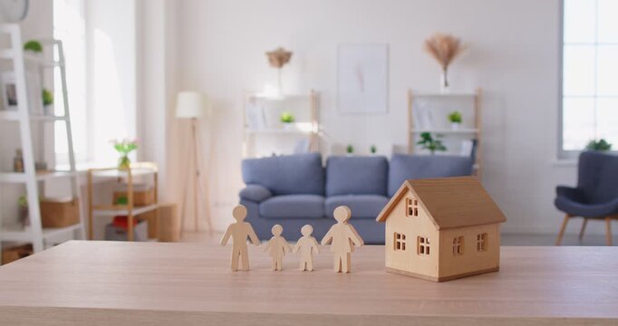 Family and House. Wooden family with two children cutout figures standing next to house model on table. Close up of human figures and house symbolizing dream of owning ones own home for families.