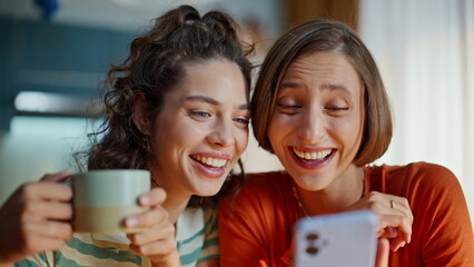 Smiling besties reading smartphone message sitting home together closeup. 