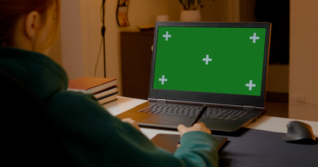 Graphic designer creating digital art on pen tablet, working with laptop and green screen backdrop for professional design project