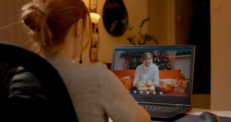 Young woman connects with a friend over a laptop during Christmas, exchanging gifts and holiday greetings while surrounded by festive decorations at home.