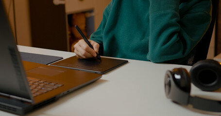 A woman passionately creating illustrations with a graphic tablet and laptop in her home office. She utilizes a stylus while focused on her artistic process.