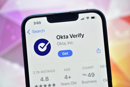 A detailed, close-up photograph focusing on a smartphone displaying the application store page for 'Okta Verify'. The screen shows the app icon, name, rating, and the 'Get' button, set against a softl